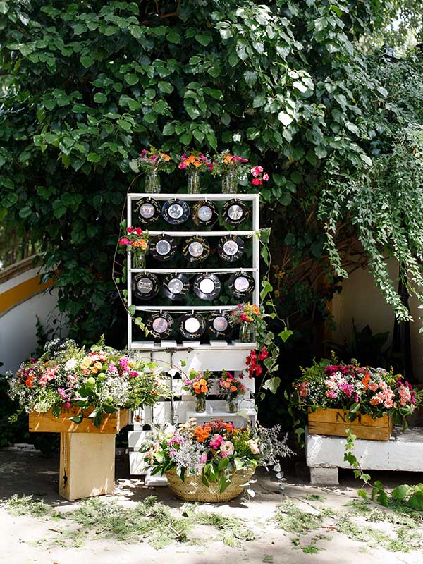 La imagen muestra el seating plan de la boda de Elena y Carlos compuesto por una estructura con discos de vinilo y centros, cajas y búcaros repletos de flores